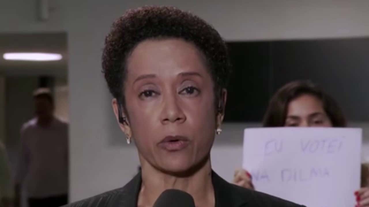 Mulher segura cartaz de protesto durante link ao vivo na Globo (Foto: Reprodução)