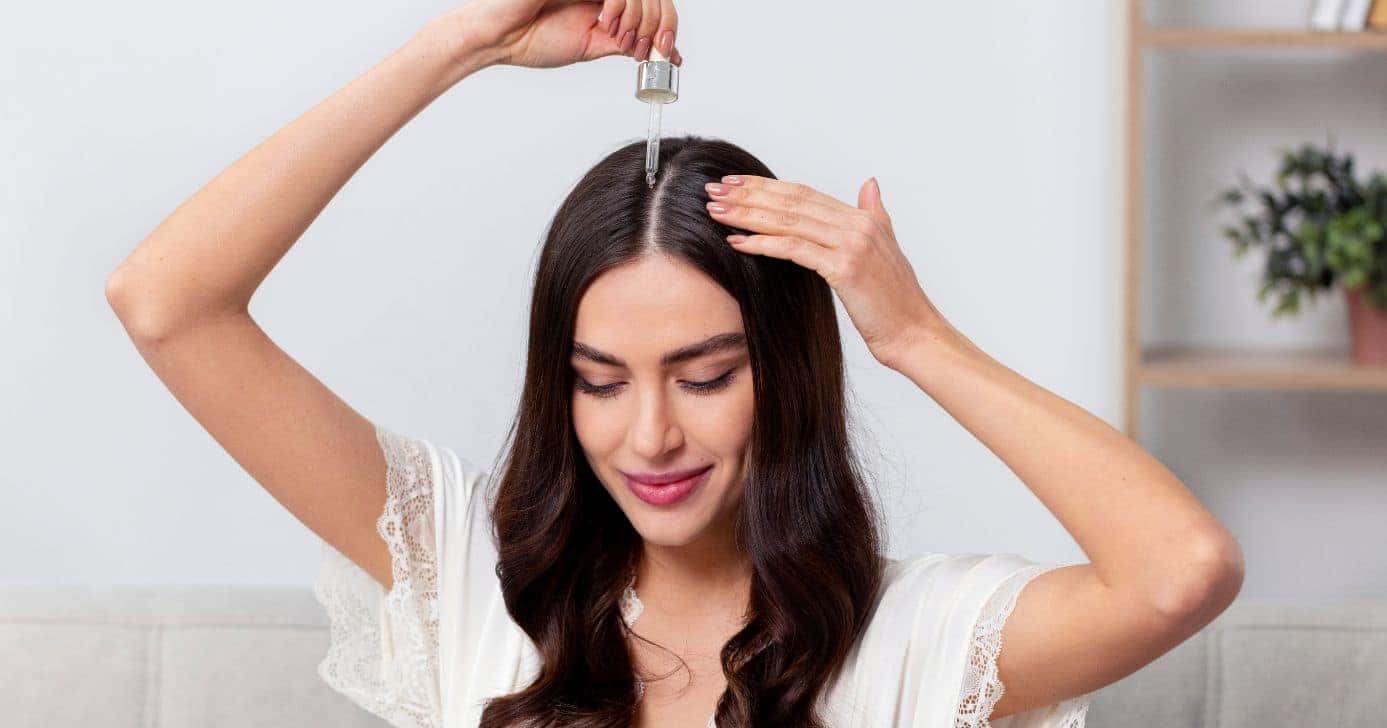 Mulher passando óleo no cabelo (Foto: Canva)