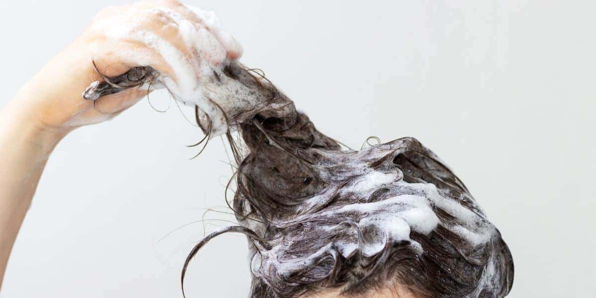 Mulher lavando o cabelo com shampoo (Reprodução: Canva)