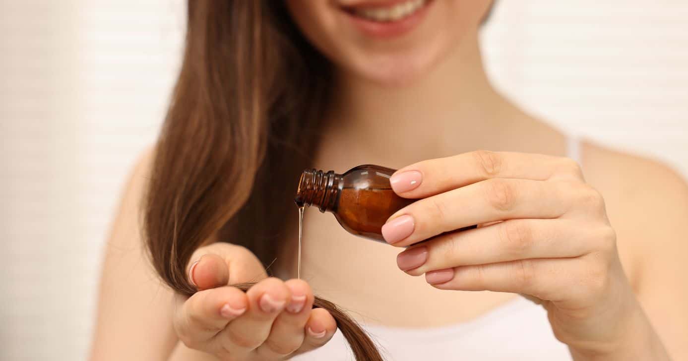 Mulher passando óleo no cabelo (Foto: Canva)