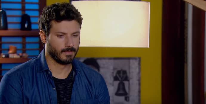 Personagem de As Aventuras de Poliana, Marcelo em cena de cabeça abaixada, ele usa camisa social azul e barba Personagem de As Aventuras de Poliana, Marcelo em cena de cabeça abaixada, ele usa camisa social azul e barba