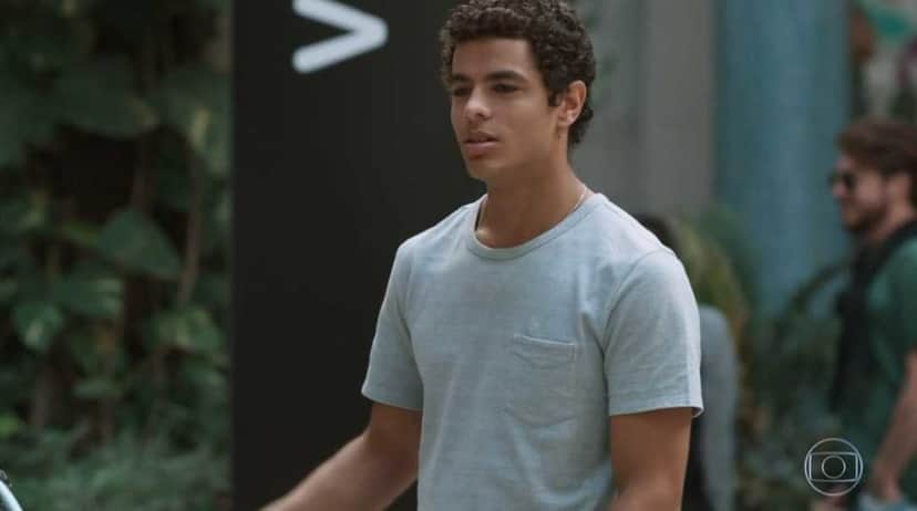 Tato da novela Malhação Viva a Diferença está em pé em área livre de camisa cinza Tato da novela Malhação Viva a Diferença está em pé em área livre de camisa cinza