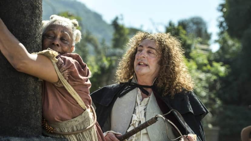 Idalina amarrada em tronco e Sebastião com chicote nas mãos a olha com repulsa em cena de Novo Mundo Idalina amarrada em tronco e Sebastião com chicote nas mãos a olha com repulsa em cena de Novo Mundo