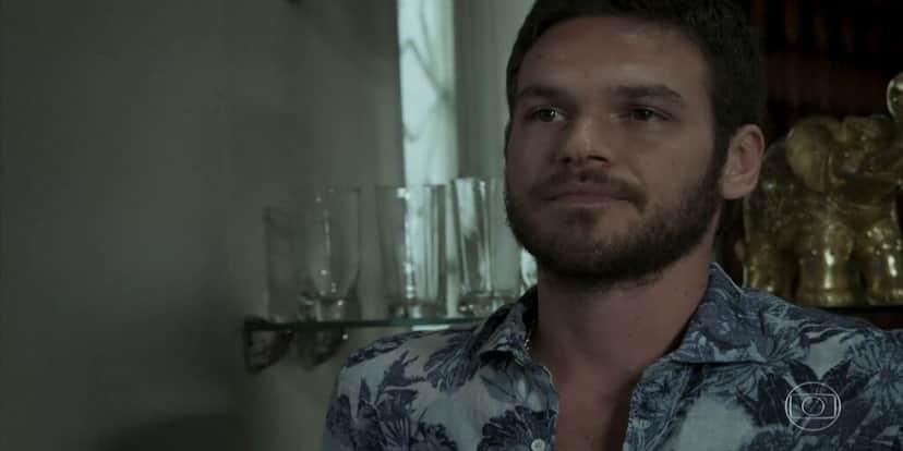 Rubinho da novela A Força do Querer olha para o lado esquerdo com expressão séria usando uma camisa branca com flores azuis Rubinho da novela A Força do Querer olha para o lado esquerdo com expressão séria usando uma camisa branca com flores azuis