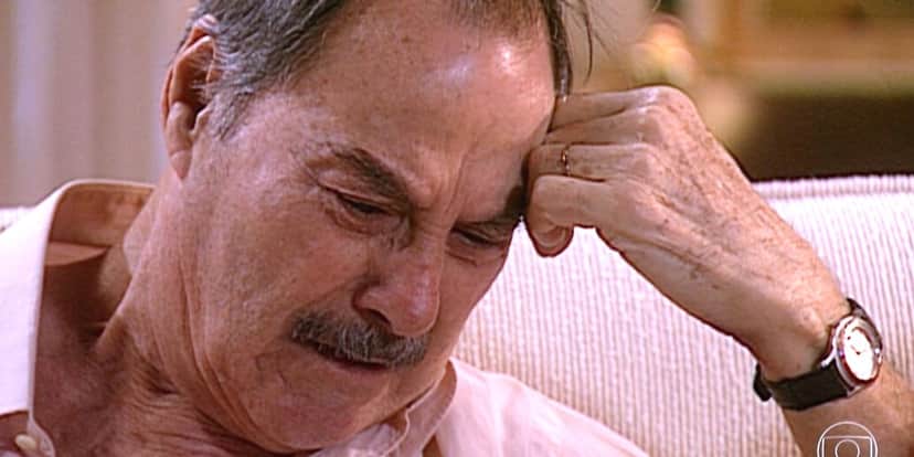 Paschoal, homem velho, branco e bigode, chora com mão encostada na sua testa em Laços de Família