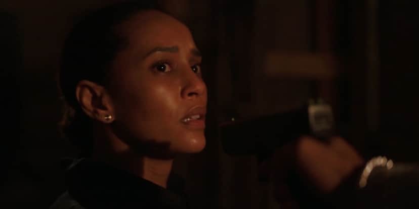 Vitória de Amor de Mãe, está em cena escura da novela com arma apontada para o seu rosto, ela é uma mulher negra que tem expressão de apreensão