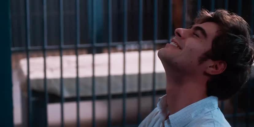 Davi está de perfil com a cabeça inclinada para trás, usa camisa branca, seu tom de pele é branco com cabelo castanho curto, ao fundo da imagem há uma grade cinza Davi está de perfil com a cabeça inclinada para trás, usa camisa branca, seu tom de pele é branco com cabelo castanho curto, ao fundo da imagem há uma grade cinza