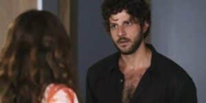 Ari veste camisa preta social aberta, barba e cabelos castanhos em cena da novela Travessia Ari veste camisa preta social aberta, barba e cabelos castanhos em cena da novela Travessia