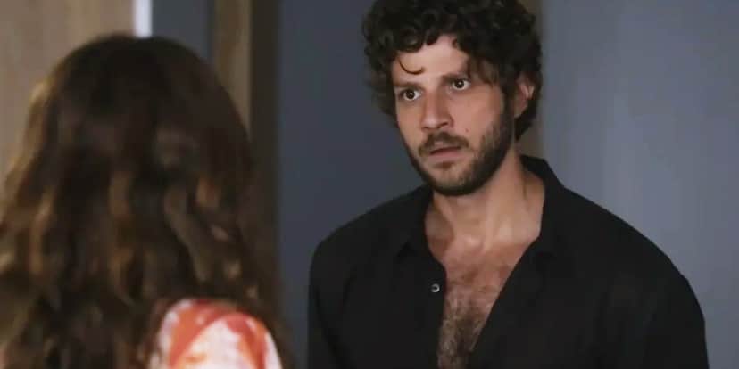 Ari veste camisa preta social aberta, barba e cabelos castanhos em cena da novela Travessia Ari veste camisa preta social aberta, barba e cabelos castanhos em cena da novela Travessia