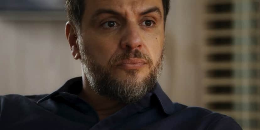 Moretti é um personagem de Travessia branco, que usa barba grande com pelos castanhos e brancos, camisa social azul e tem expressão séria Moretti é um personagem de Travessia branco, que usa barba grande com pelos castanhos e brancos, camisa social azul e tem expressão séria