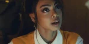 Talita na trama de Travessia usando uma camisa branca, colete laranja e com expressão de surpresa Talita na trama de Travessia usando uma camisa branca, colete laranja e com expressão de surpresa