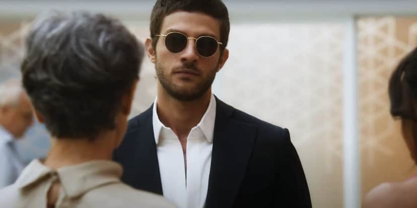 Ari usando terno azul, camisa branca e óculos em cena da novela Travessia Ari usando terno azul, camisa branca e óculos em cena da novela Travessia