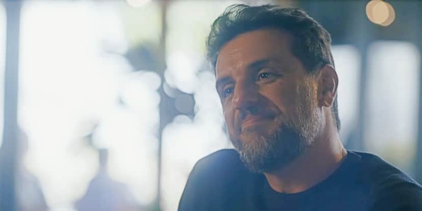 Moretti em cena da novela Travessia usando camisa cinza escuro Moretti em cena da novela Travessia usando camisa cinza escuro