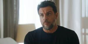 Moretti em cena da novela Travessia sentado na cama usando camisa preta Moretti em cena da novela Travessia sentado na cama usando camisa preta