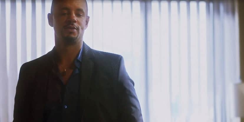 Orfeu em cena da novela Vai na Fé é um homem negro que usa terno azul escuro assim como camisa Orfeu em cena da novela Vai na Fé é um homem negro que usa terno azul escuro assim como camisa