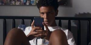 Theo sentado na cama segurando celular em cena da novela Travessia Theo sentado na cama segurando celular em cena da novela Travessia
