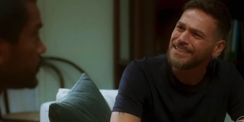 Theo em cena da novela Vai na Fé sentado em sofá e usando camisa preta Theo em cena da novela Vai na Fé sentado em sofá e usando camisa preta