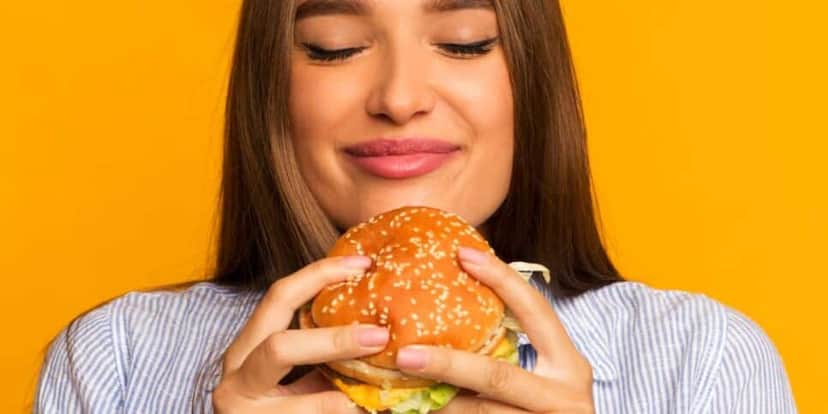 Mulher comendo hambúrguer (Foto: Canva) Mulher comendo hambúrguer (Foto: Canva)