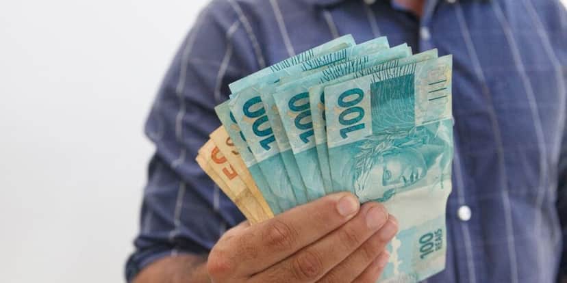 Homem segurando notas de cem e cinquenta reais (Foto: Canva)