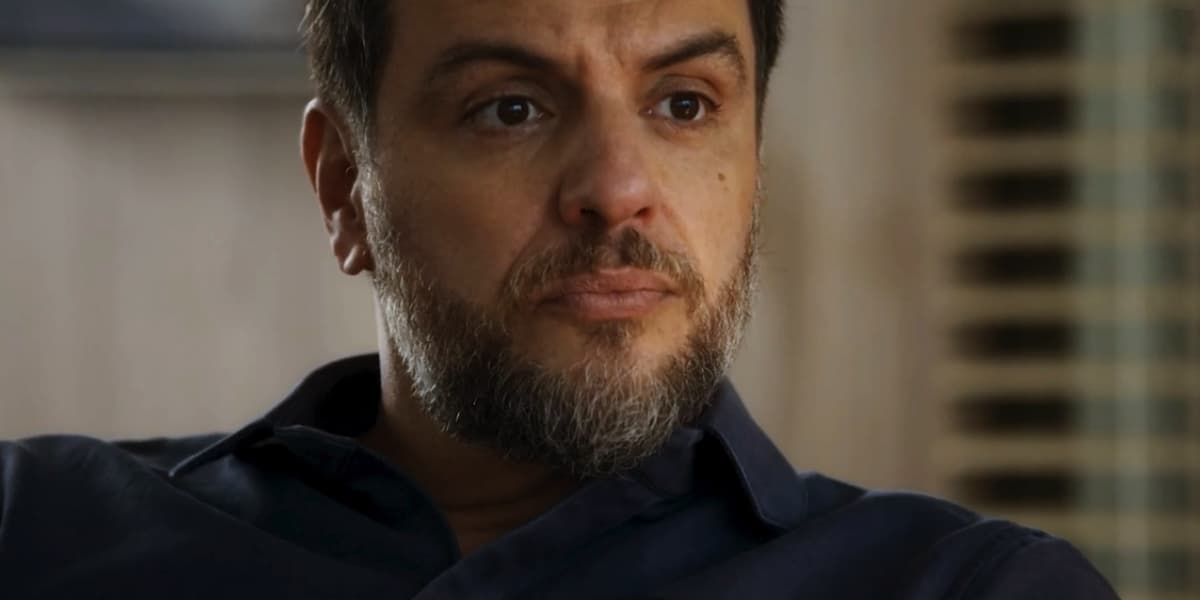 Moretti é um personagem de Travessia branco, que usa barba grande com pelos castanhos e brancos, camisa social azul e tem expressão séria Moretti é um personagem de Travessia branco, que usa barba grande com pelos castanhos e brancos, camisa social azul e tem expressão séria