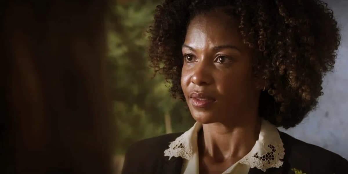 Dagmar é uma mulher negra, com cabelo blackpower médio que usa blazer preto e camisa branca em cena da novela Mar do Sertão Dagmar é uma mulher negra, com cabelo blackpower médio que usa blazer preto e camisa branca em cena da novela Mar do Sertão