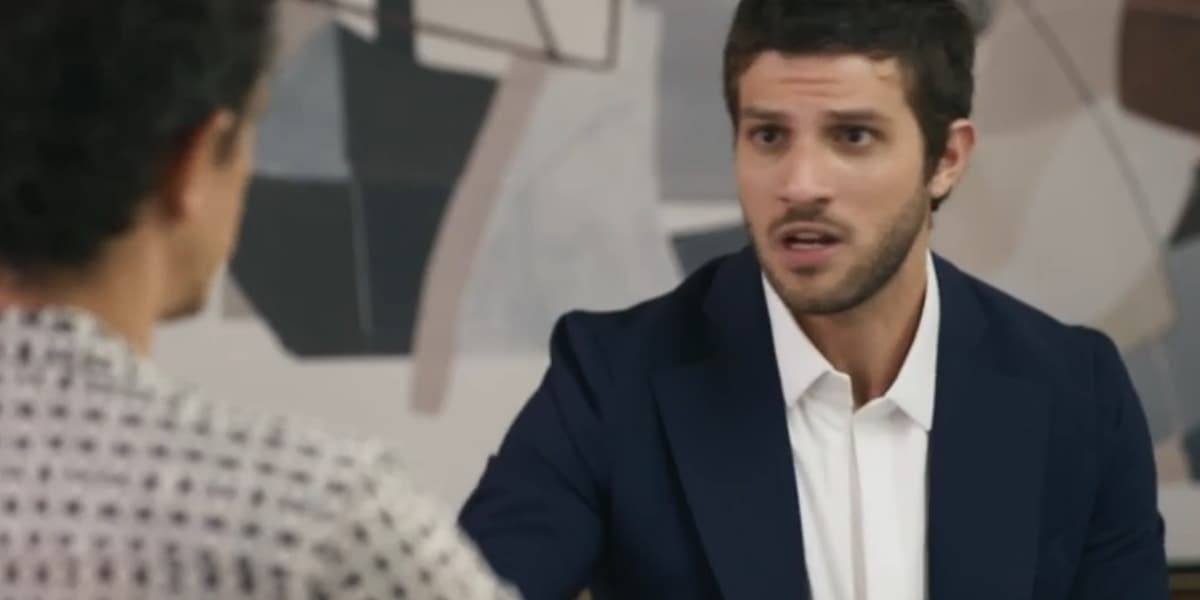 Ari usando terno azul escuro e camisa branca em cena da novela Travessia Ari usando terno azul escuro e camisa branca em cena da novela Travessia