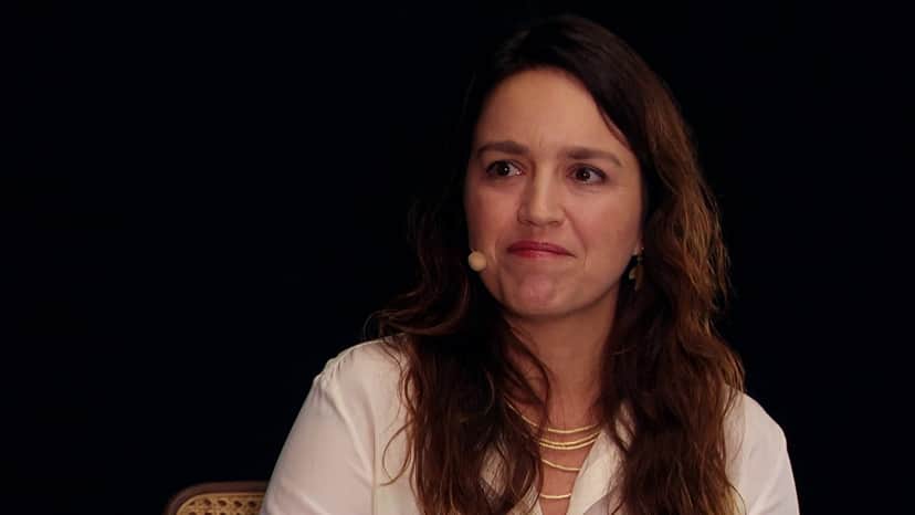 Autora Manuela Dias de Amor de Mãe usa blusa branca, microfone de bolinha e cabelos longos e castanhos Autora Manuela Dias de Amor de Mãe usa blusa branca, microfone de bolinha e cabelos longos e castanhos