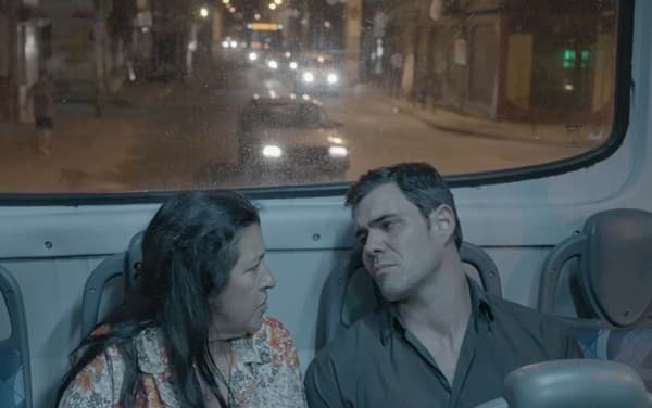 Na imagem da novela Amor de Mãe, Regina Casé (Lurdes) de camisa florida e Juliano Cazarré (Magno) com camisa social escura estão sentados em um ônibus à noite no Rio de Janeiro Na imagem da novela Amor de Mãe, Regina Casé (Lurdes) de camisa florida e Juliano Cazarré (Magno) com camisa social escura estão sentados em um ônibus à noite no Rio de Janeiro