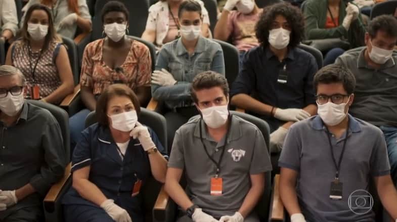 Pessoas diversas estão sentadas em um mini teatro em cena de Salve-se Quem Puder usando máscaras nos rostos e luvas Pessoas diversas estão sentadas em um mini teatro em cena de Salve-se Quem Puder usando máscaras nos rostos e luvas