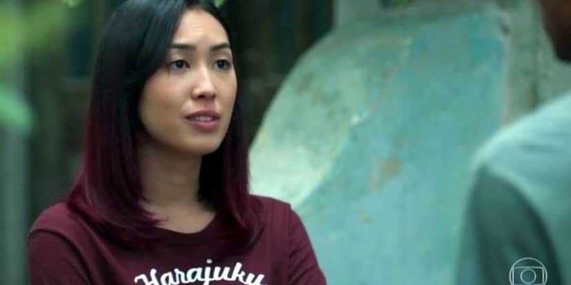 Na imagem, Tina de Malhação - Viva a Diferença é uma jovem japonesa com camisa rosa e cabelo multicolor entre preto e roxo Na imagem, Tina de Malhação - Viva a Diferença é uma jovem japonesa com camisa rosa e cabelo multicolor entre preto e roxo