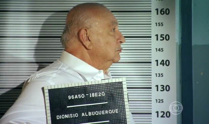 Dionísio de perfil com placa com o nome Dionísio Albuquerque em cena de Flor do Caribe Dionísio de perfil com placa com o nome Dionísio Albuquerque em cena de Flor do Caribe