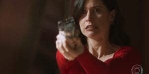 Regina usa vestido vermelho e segura uma arma em cena da novela Cara e Coragem Regina usa vestido vermelho e segura uma arma em cena da novela Cara e Coragem