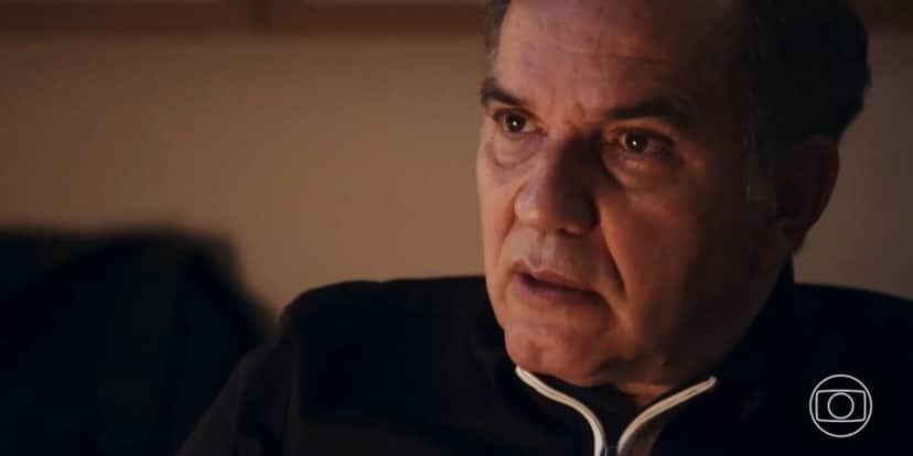 Guerra homem branco usando blusa de frio azul escura com detalhe no zíper em branco com expressão chocada em cena da novela Travessia Guerra homem branco usando blusa de frio azul escura com detalhe no zíper em branco com expressão chocada em cena da novela Travessia