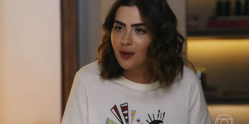 Chiara usa camiseta branca com desenhos e cabelo curto castanho com cachos em cena de Travessia Chiara usa camiseta branca com desenhos e cabelo curto castanho com cachos em cena de Travessia