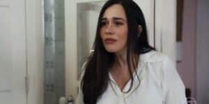 Guida é uma mulher branca, que usa cabelo longo liso preto e uma camiseta social branca e está em cena da novela Travessia Guida é uma mulher branca, que usa cabelo longo liso preto e uma camiseta social branca e está em cena da novela Travessia