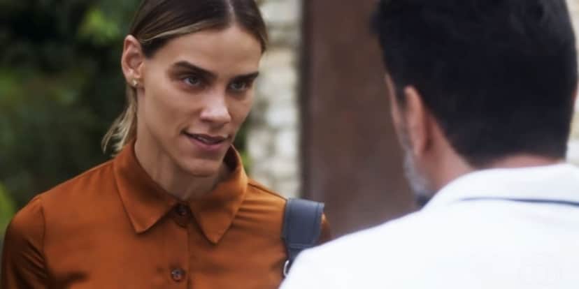 Sara usa camisa laranja e cabelo louro amarrado e conversa com Moretti de costa usando camisa branca na novela Travessia Sara usa camisa laranja e cabelo louro amarrado e conversa com Moretti de costa usando camisa branca na novela Travessia