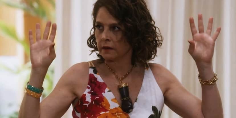 Núbia em cena da novela Travessia usando vestido florido e colar com grande mão preta com punho fechado Núbia em cena da novela Travessia usando vestido florido e colar com grande mão preta com punho fechado