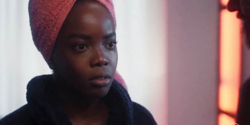Em Vai na Fé, Kate (Clara Moneke) usa roupão azul escuro, toalha rosa amarrada na cabeça e demonstra apreensão Em Vai na Fé, Kate (Clara Moneke) usa roupão azul escuro, toalha rosa amarrada na cabeça e demonstra apreensão