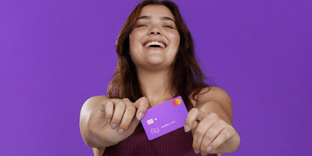 Pessoa feliz segurando cartão do Nubank (Foto: Reprodução / site do banco) Pessoa feliz segurando cartão do Nubank (Foto: Reprodução / site do banco)