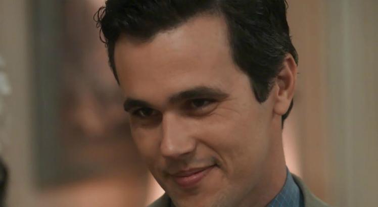Fundo desfocado, ator sorri em cena na novela "Tempo de Amar"